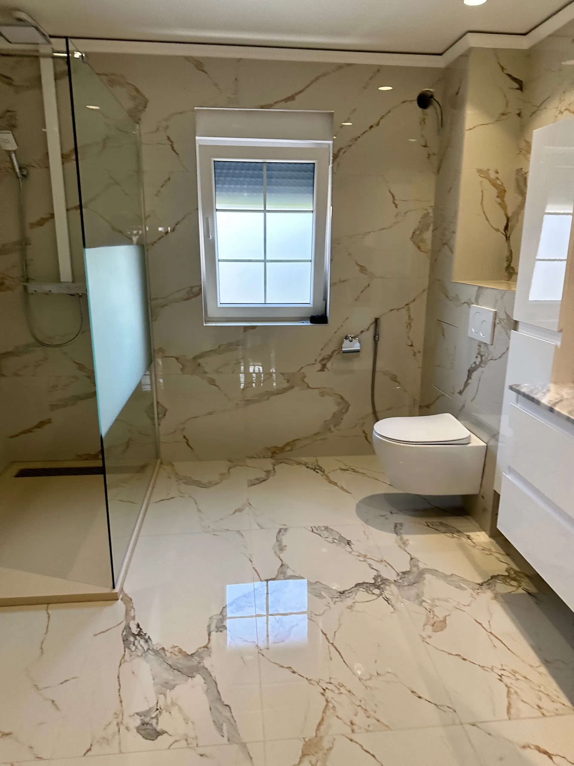 Salle de bain terminée aux carreaux effet marbre posés en miroir, WC suspendu et fenêtre dépolie.