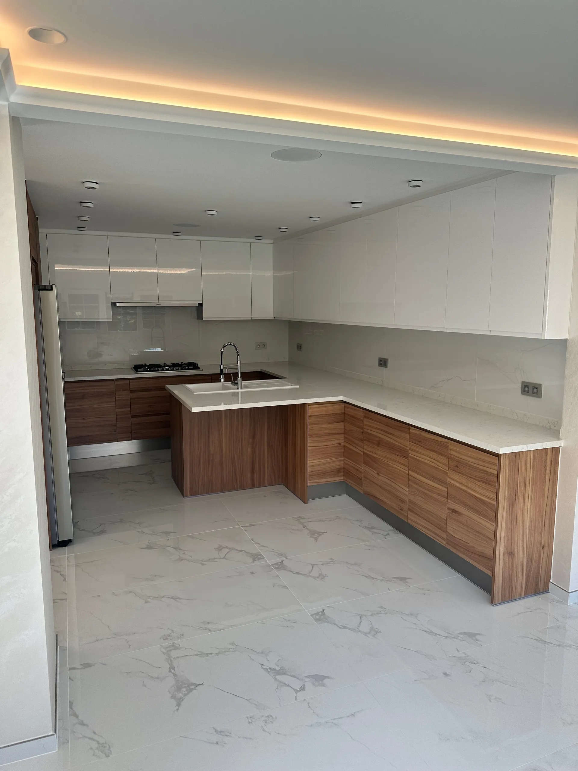 Cuisine en U avec meubles hauts blancs brillants, meubles bas ton bois, plan de travail blanc avec évier et plaque de cuisson au gaz