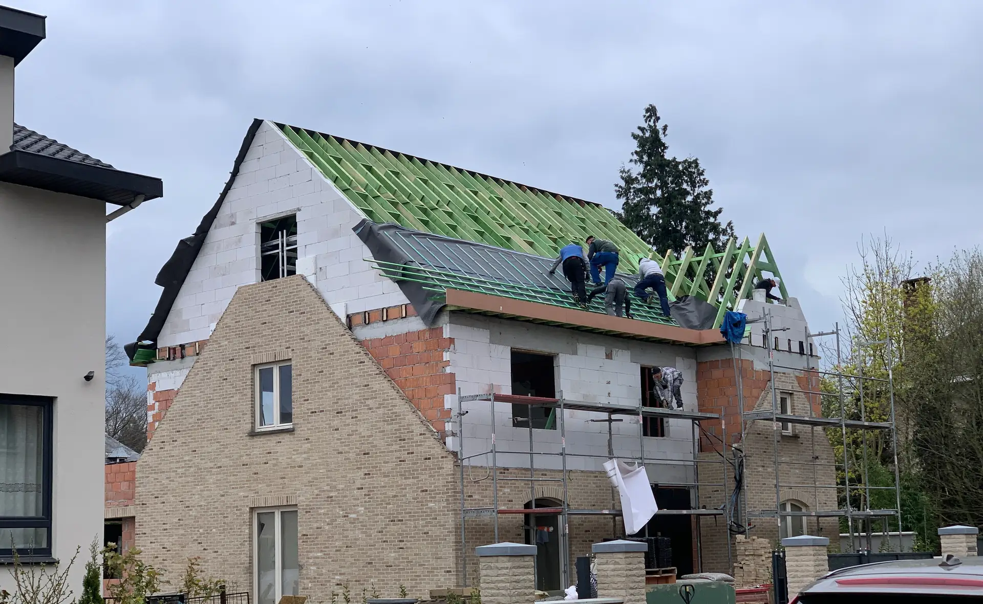 Une équipe de couvreurs pose le sous-toiture et les liteaux sur la nouvelle charpente de l'étage ajouté, échafaudage le long de la façade